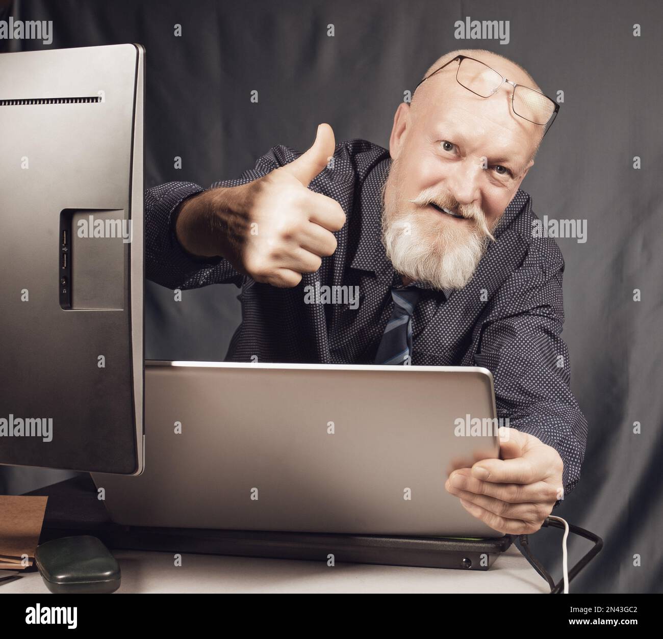 Travail au bureau, un homme âgé gai avec une barbe grise devant un ordinateur portable est satisfait du résultat. Banque D'Images
