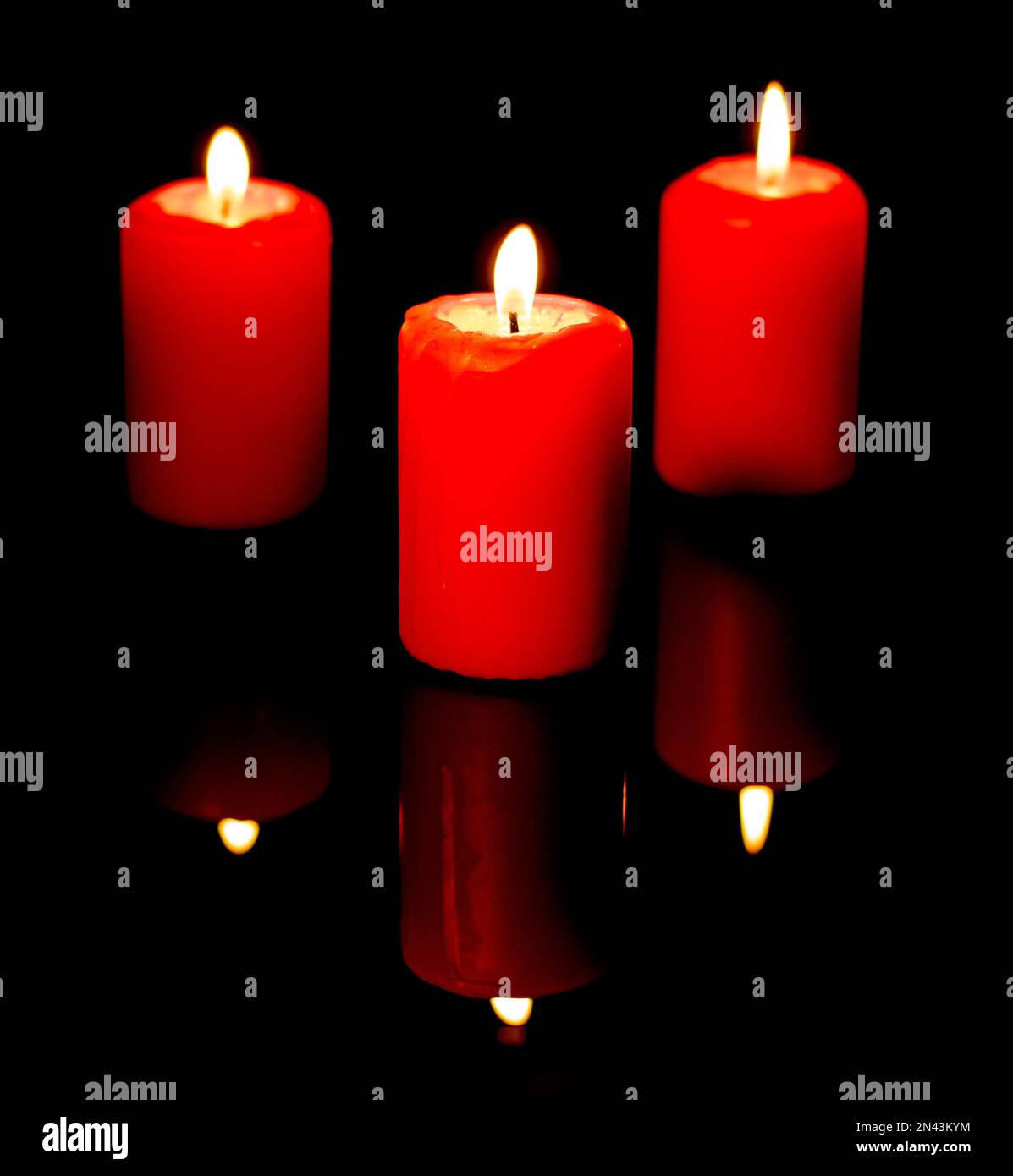 Trois bougies rouges allumées sont reflétées dans un fond miroir noir. Banque D'Images