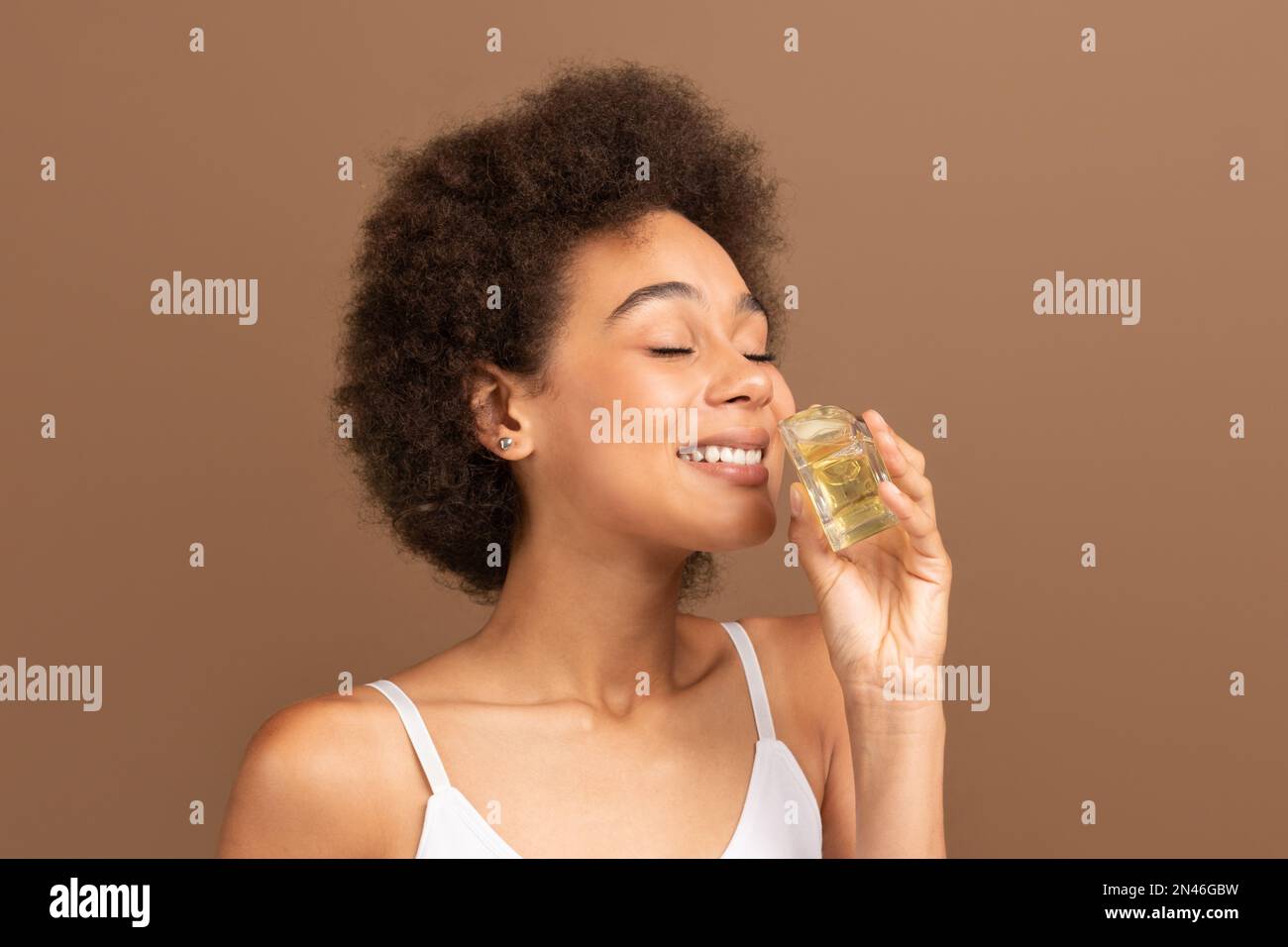 Gaie jeune afro-américaine curly femme avec la peau parfaite en haut blanc sniffing bouteille de parfum Banque D'Images