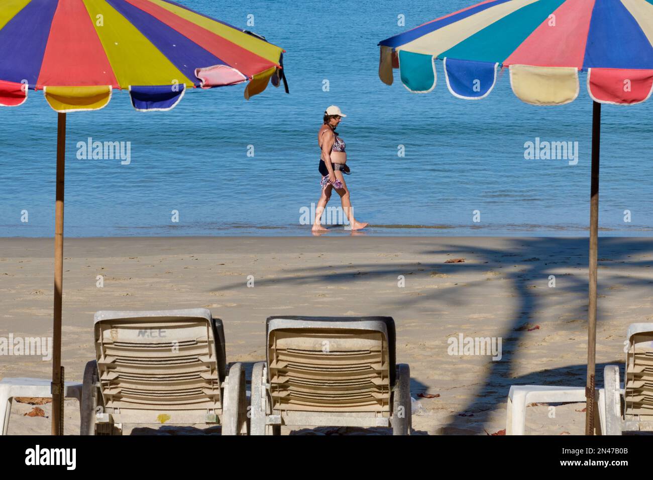 En début de matinée, une femme de l'Ouest marche le long de la plage de Kamala à Phuket, en Thaïlande, des chaises longues et des parasols de plage en premier plan Banque D'Images