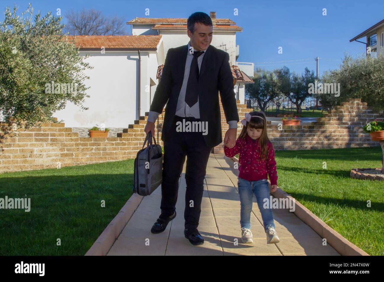 Image d'un homme d'affaires élégant revenant du travail sur son allée tenant la main d'une adorable petite fille. Amour et acceptation de la fille Banque D'Images