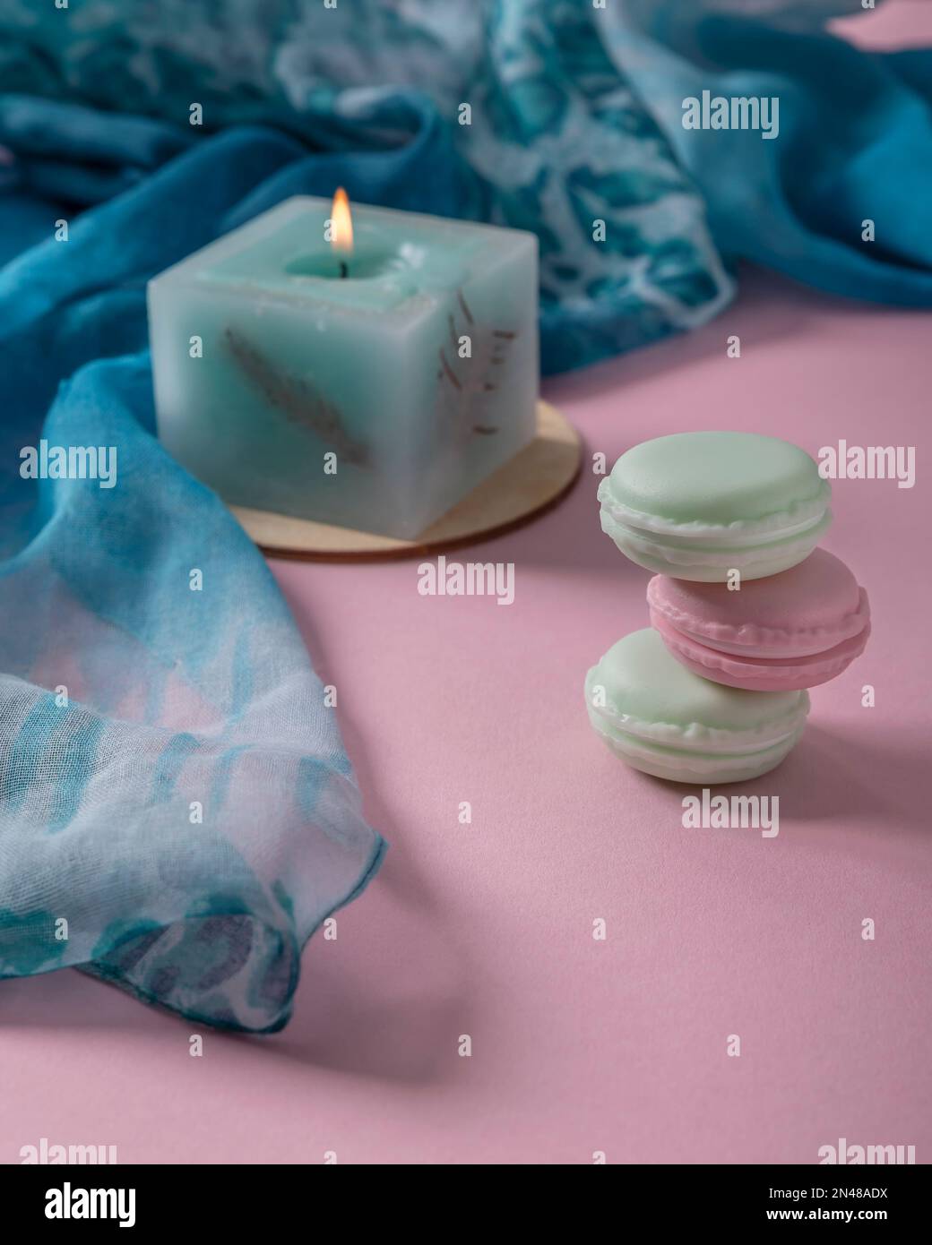Trois macarons empilés de manière crookée, une bougie allumée et un foulard, tous caractérisés par des couleurs pastel délicates Banque D'Images