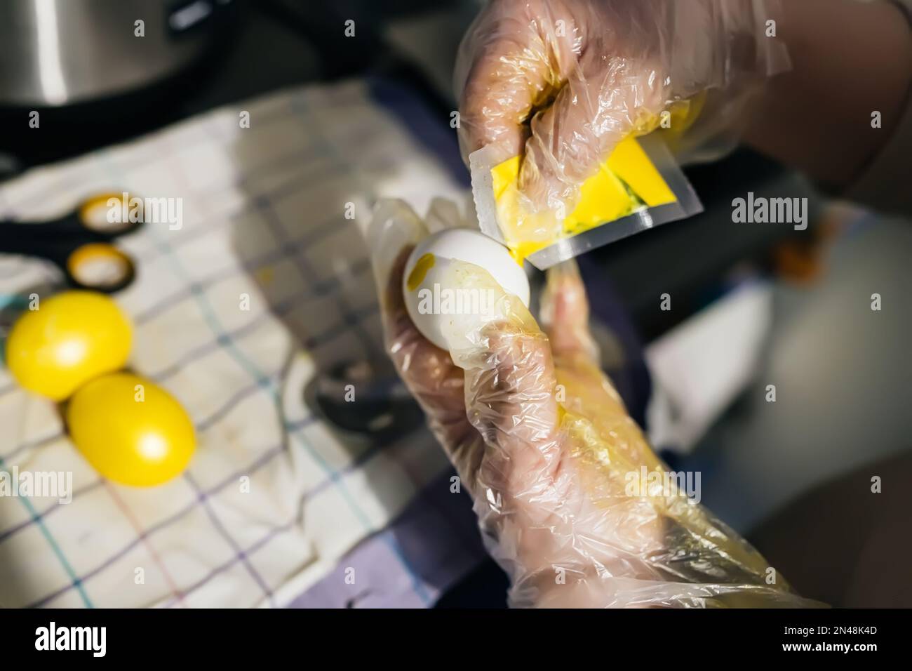 Peindre des oeufs pour Pâques avec des teintures artificielles en jaune. Les mains en gants de polyéthylène tiennent un œuf de poulet recouvert de peinture du sachet. Fait partie du Banque D'Images