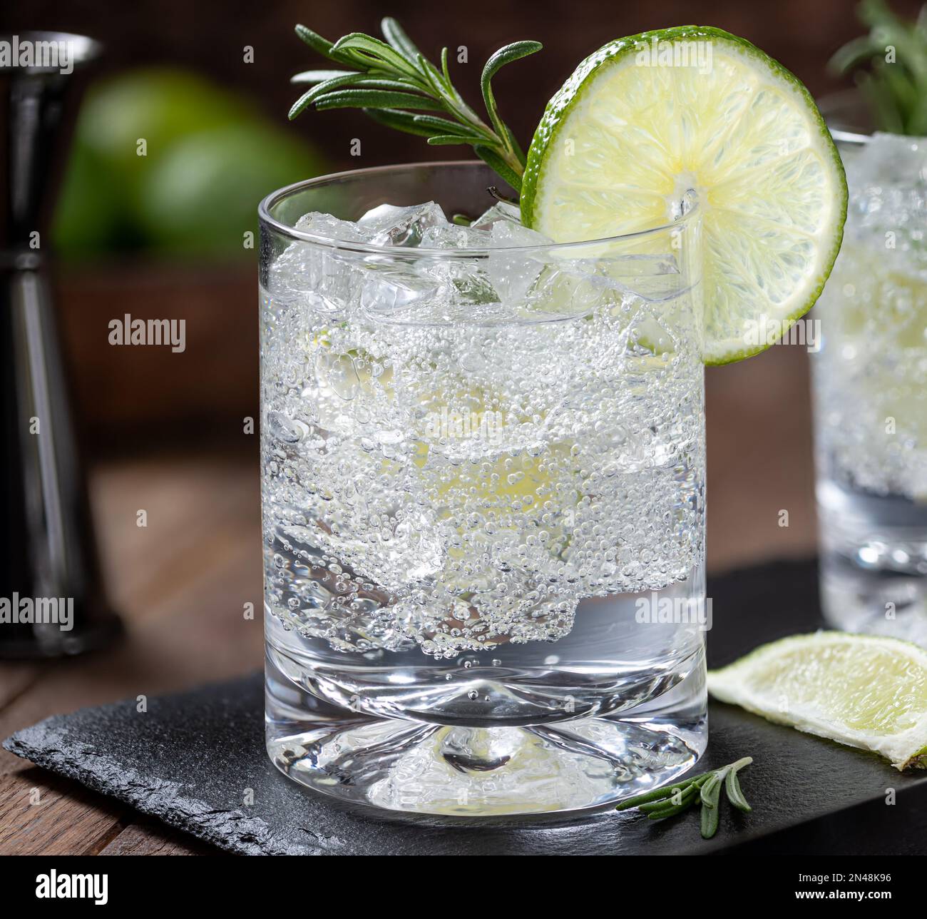 Gros plan du gin et de la boisson tonique pour cocktail avec des tranches de citron vert, du romarin et de la glace sur un panneau d'ardoise noire Banque D'Images