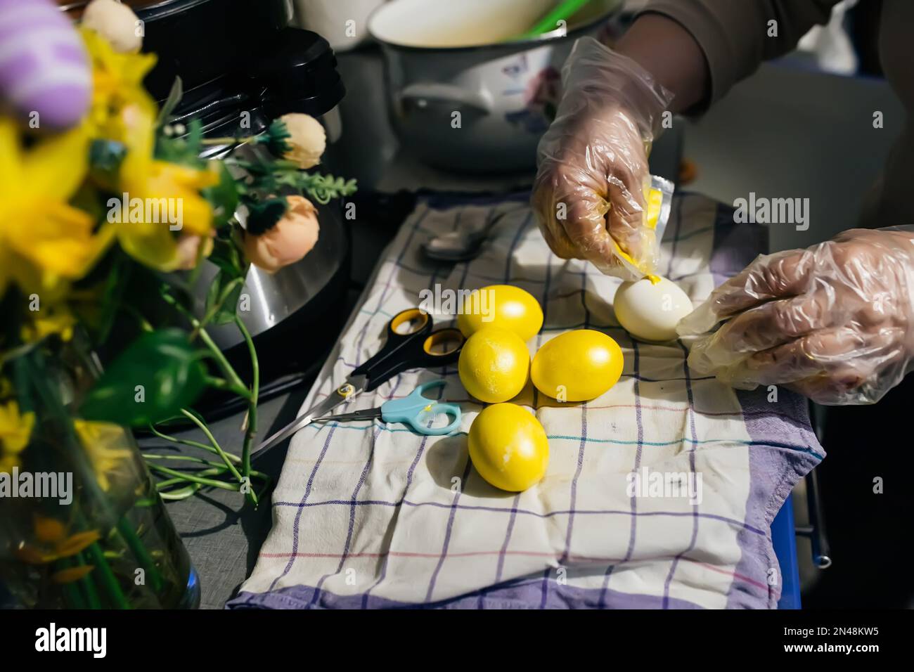 Les mains gantées essorent la peinture du sac sur l'œuf de poulet en vue de pâques. Peinture des oeufs avant les vacances. Préparation de Pâques à Banque D'Images