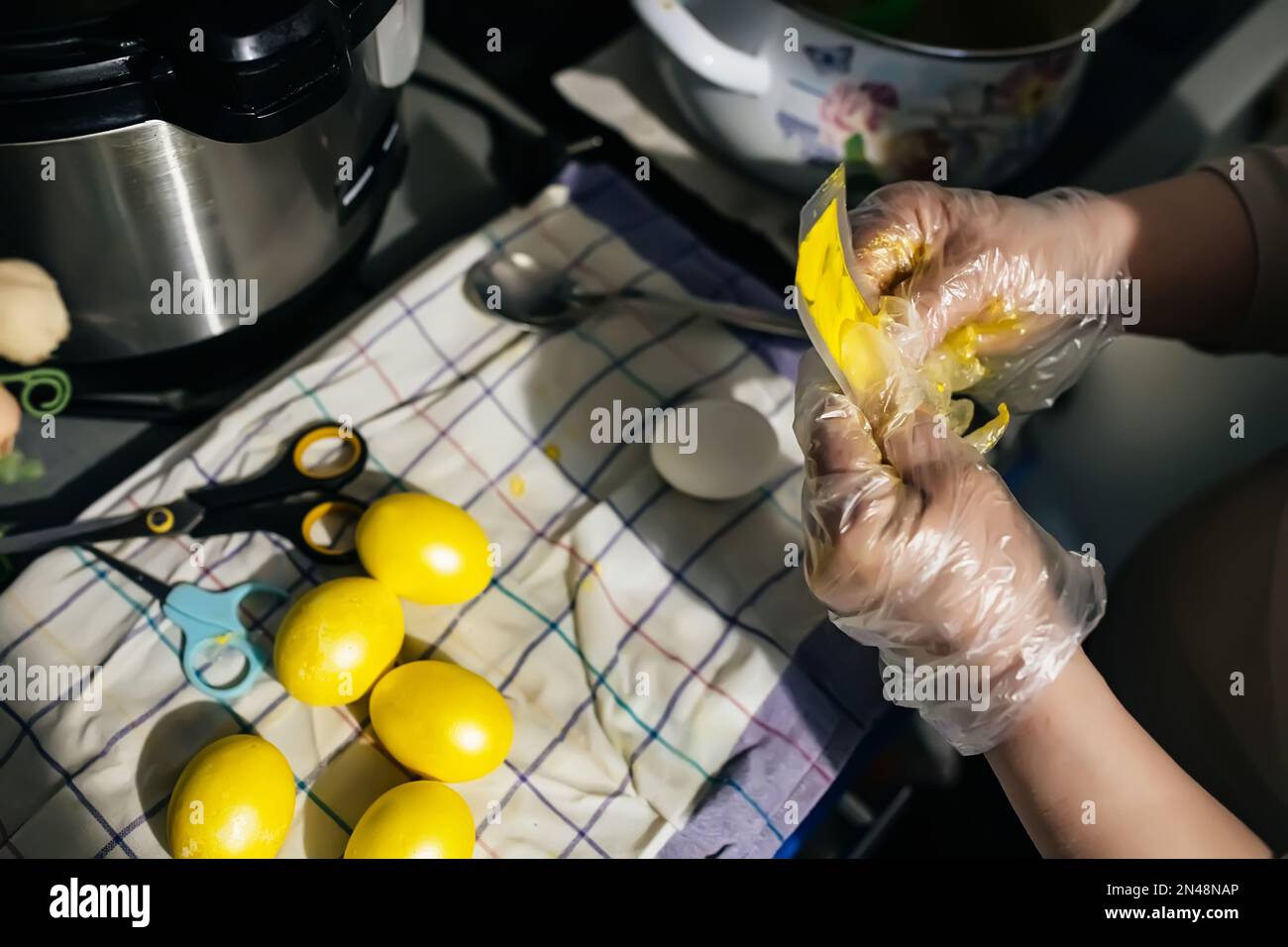 Les mains gantées essorent la peinture du sac sur l'œuf de poulet en vue de pâques. Peinture des oeufs avant les vacances. Préparation de Pâques à Banque D'Images