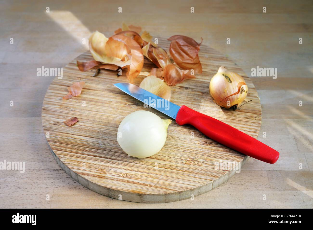 Oignon pelé et un couteau de cuisine rouge sur une planche à découper sur un plan de travail en bois, préparation pour la cuisson, espace de copie, mise au point sélectionnée, profondeur étroite de fie Banque D'Images