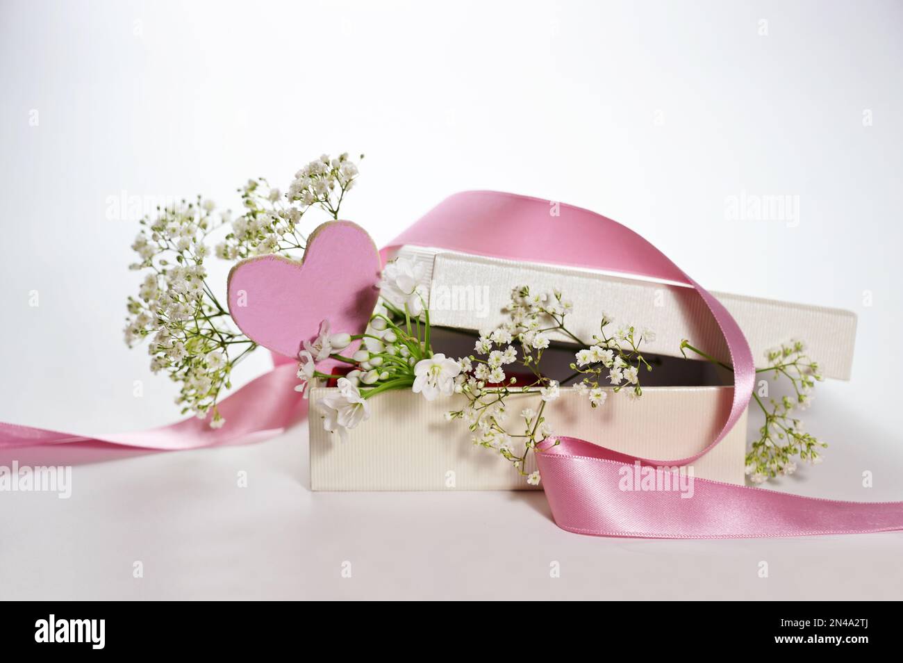 Boîte cadeau avec un coeur peint rose, un ruban et des fleurs de gitsophila blanches comme carte de vœux romantique pour les vacances, fond clair, espace de copie, Banque D'Images