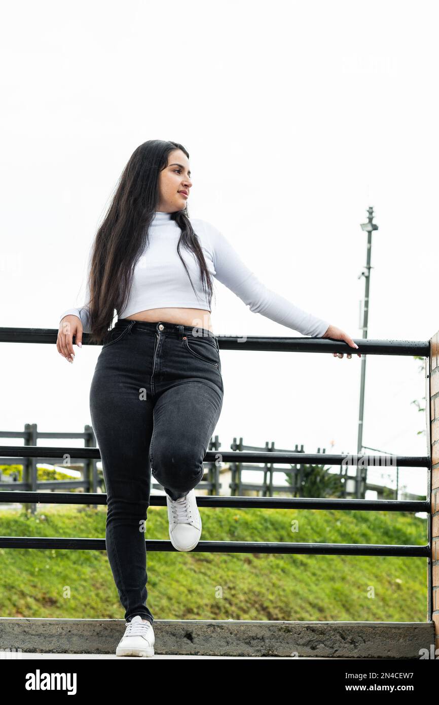 latina fille, s'appuyant sur la main courante noire, attendant détendu. fond ciel blanc Banque D'Images
