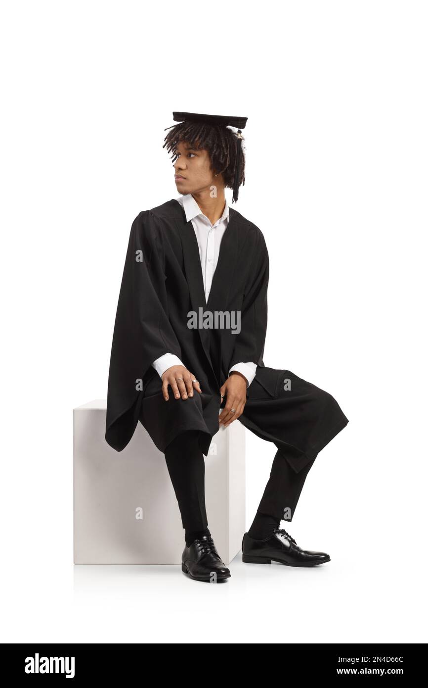 Un étudiant afro-américain diplômé dans une robe assis et regardant dans le dos isolé sur fond blanc Banque D'Images