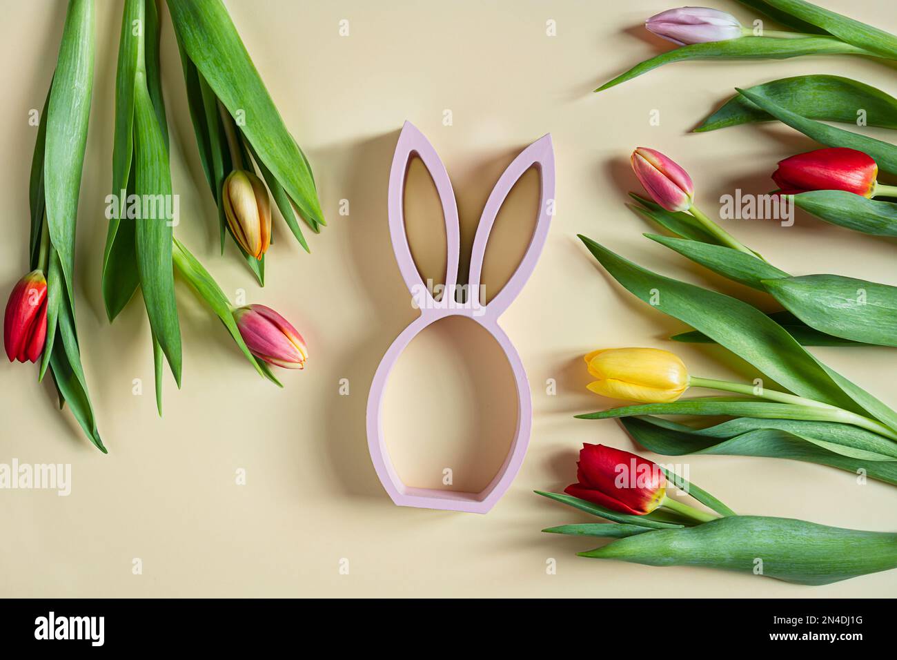 Statuette de lapin de Pâques et tulipes de printemps sur fond jaune, concept de pâques minimal, vue du dessus Banque D'Images