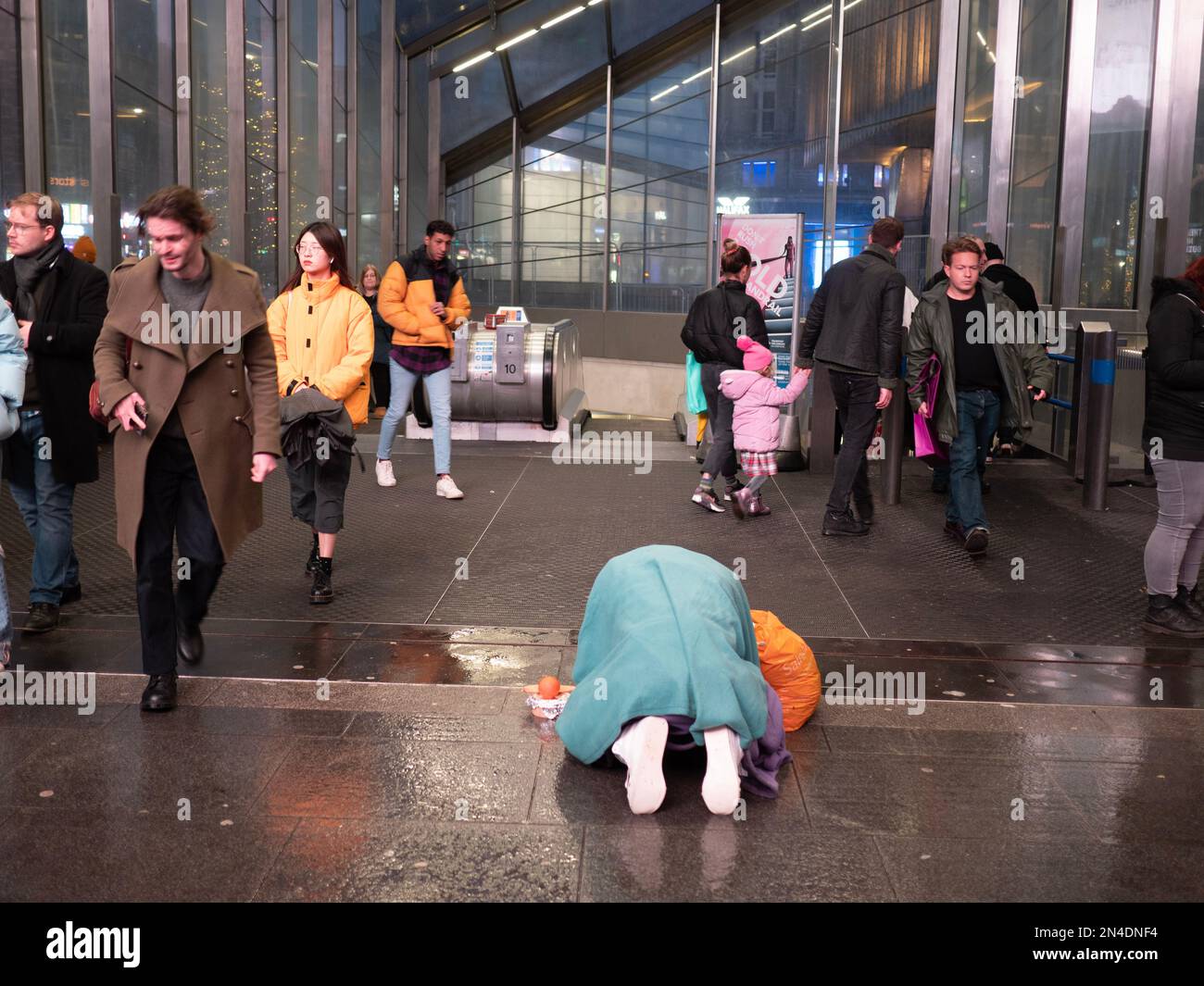 Un homme sans domicile imploré pour de l'argent comptant prostrate sur un sol humide, devant la station de métro très fréquentée dans le centre de Londres Banque D'Images