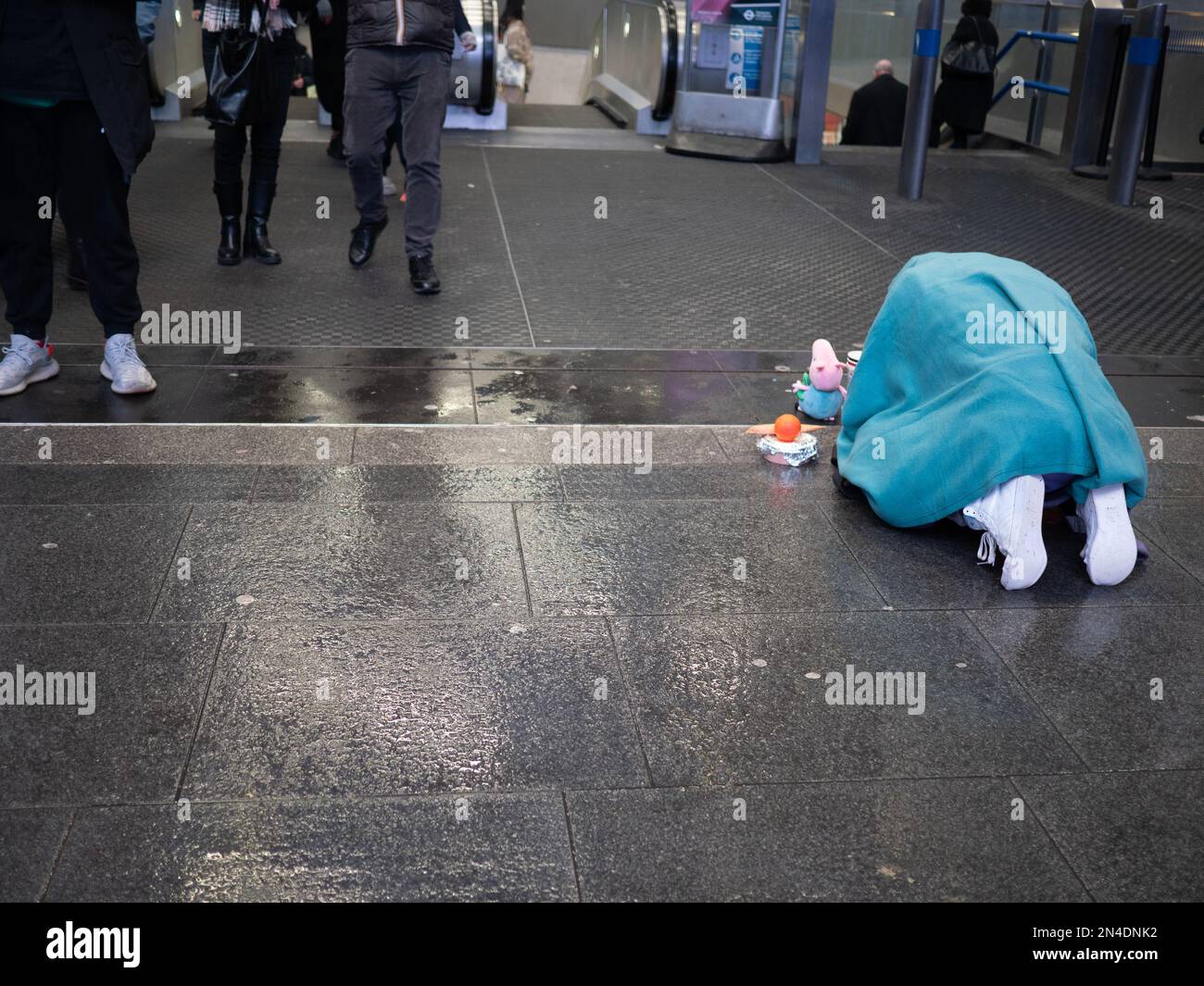 Un homme sans domicile imploré pour de l'argent comptant prostrate sur un sol humide, devant la station de métro très fréquentée dans le centre de Londres Banque D'Images