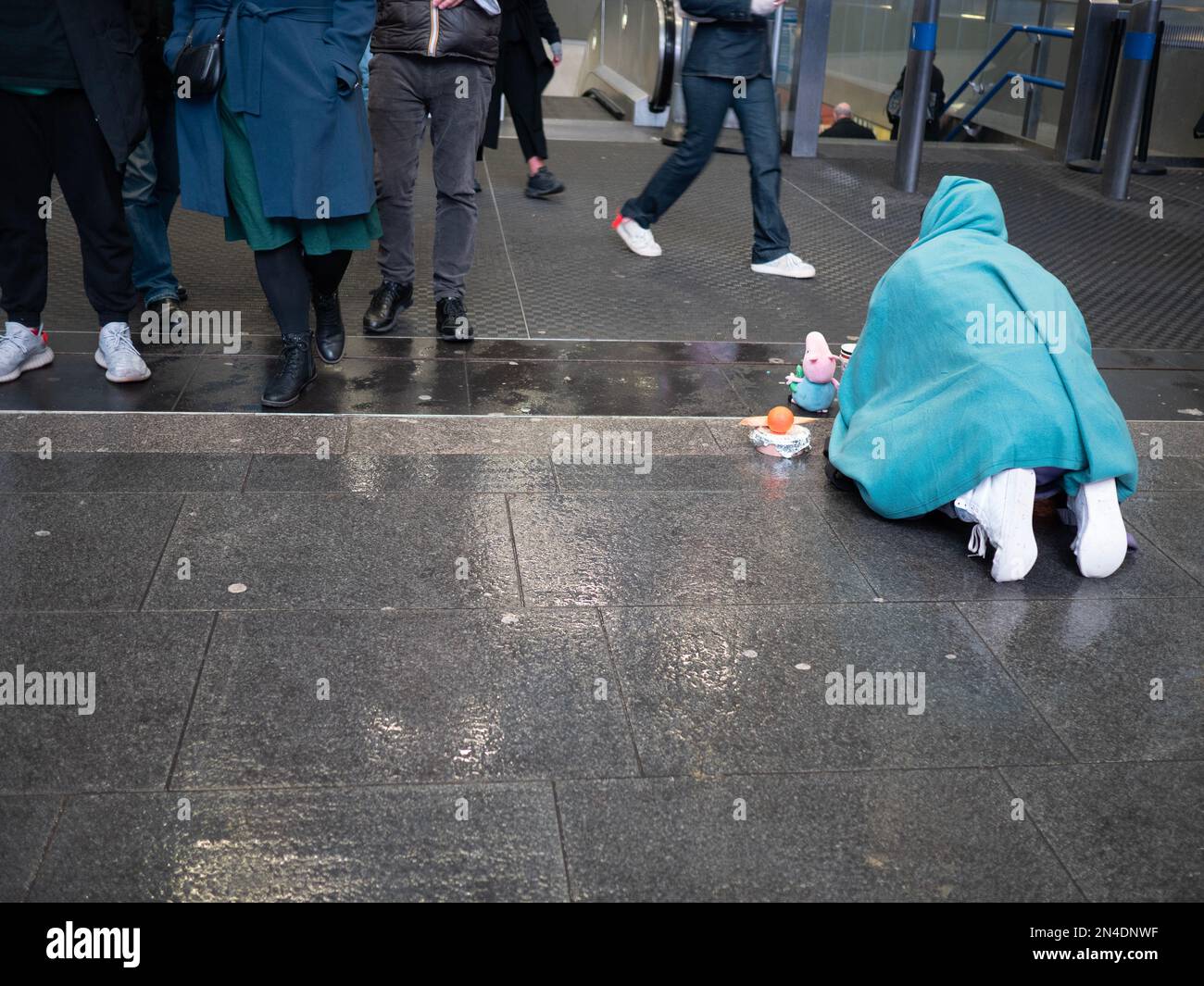 Un homme sans domicile imploré pour de l'argent comptant prostrate sur un sol humide, devant la station de métro très fréquentée dans le centre de Londres Banque D'Images