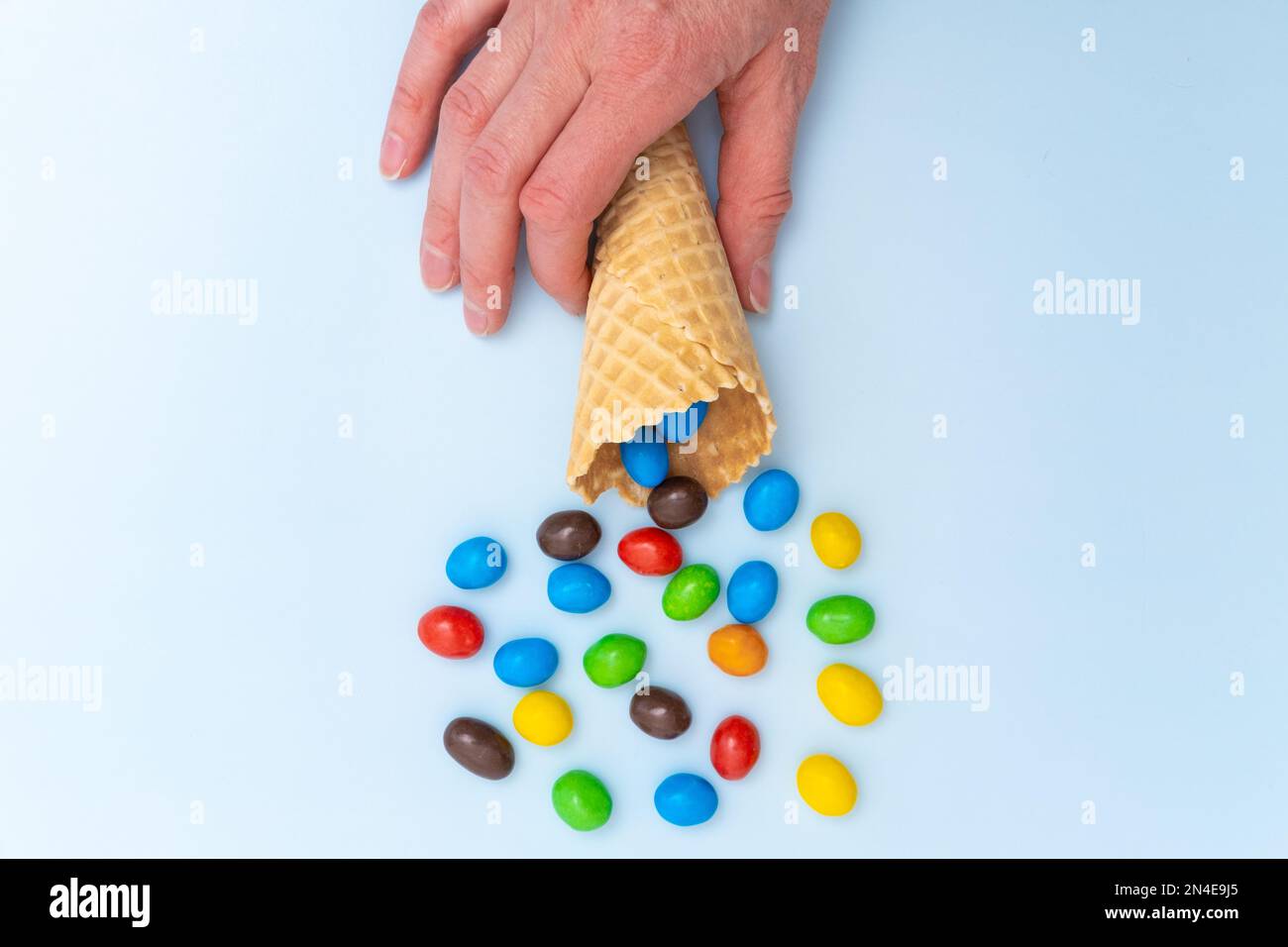 Une main tenant un cône de gaufre vide avec des bonbons ronds multicolores dispersés, des dragées. Des vacances amusantes. Bonbons pour enfants. Banque D'Images