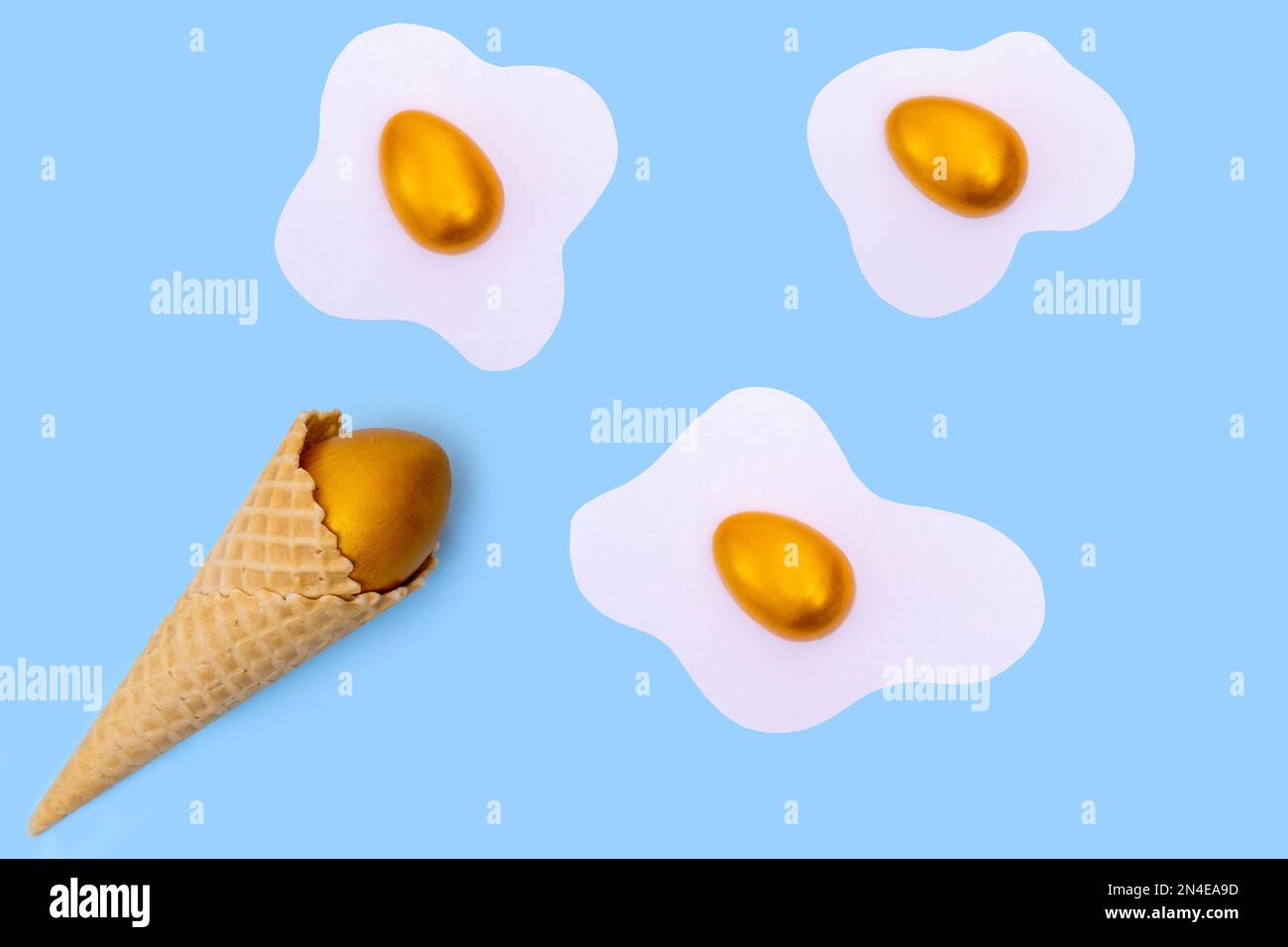 Cornet de glace à gaufres avec un œuf de Pâques doré caché et des œufs brouillés avec des œufs de couleur comme des nuages sur un fond bleu, concept, disposition plate, min Banque D'Images