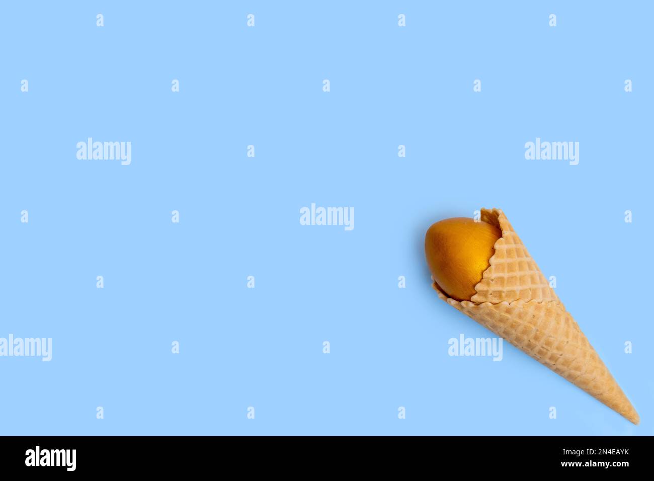 Cornet de glace gaufrée avec œuf de Pâques doré sur fond bleu, concept, espace de copie, plat. Carte de vœux de Pâques minimaliste. Banque D'Images