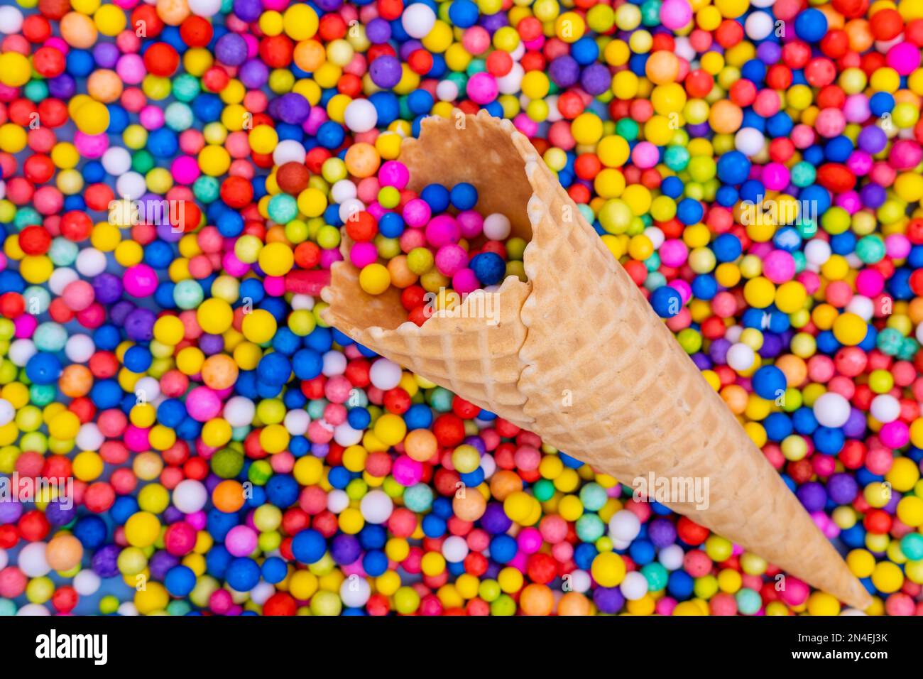 Un cône de gaufres vide avec des bonbons ronds multicolores, des dragées. Des vacances amusantes. Bonbons pour enfants. Ambiance festive et gaie. Banque D'Images