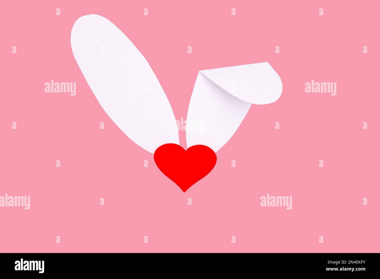Carte de vœux créative. Imitation du lapin de Pâques. Un coeur rouge au lieu d'un nez et des oreilles de papier blanc sur un fond rose. Le concept minimum de Banque D'Images