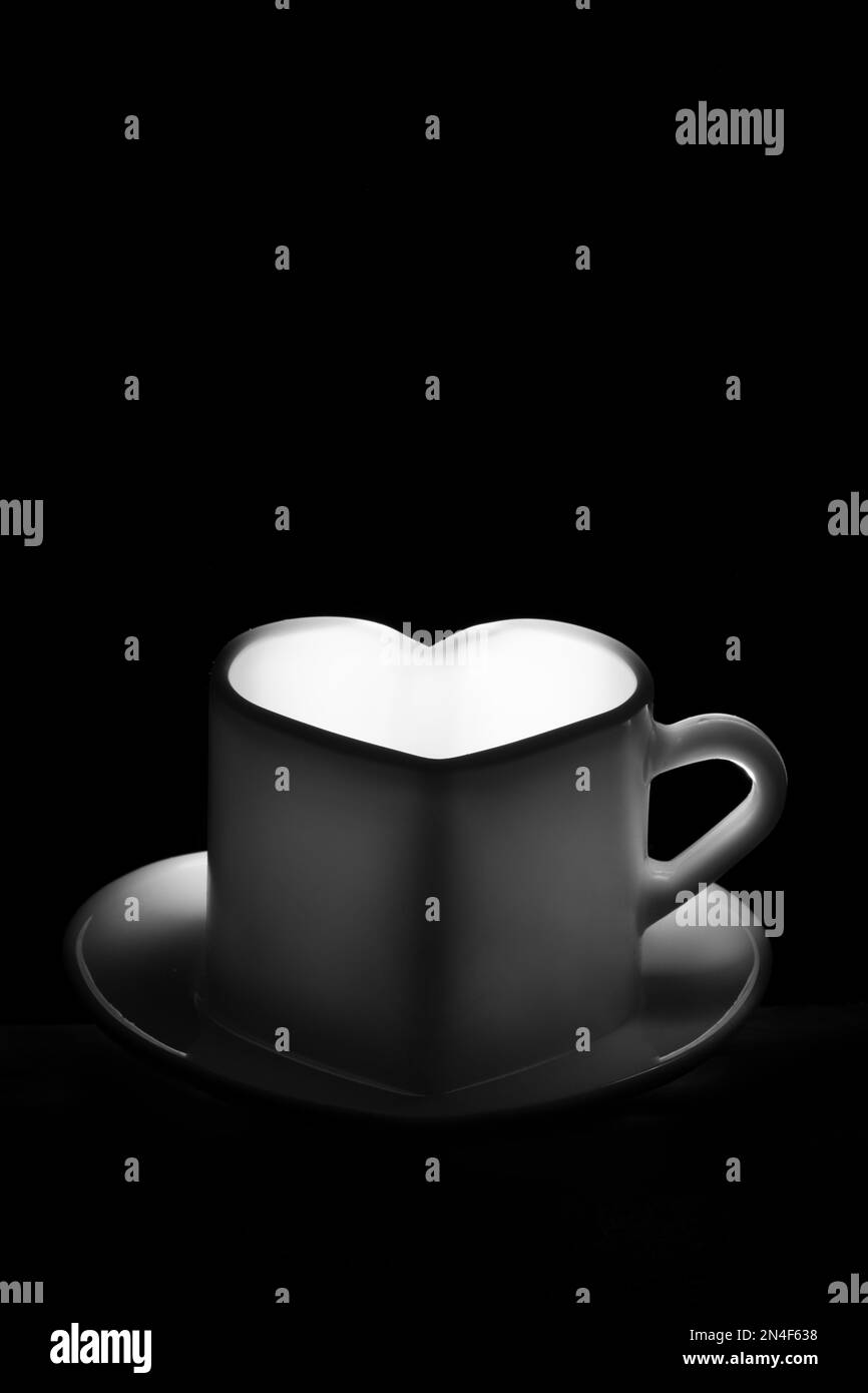 Un mug blanc en forme de coeur avec une boisson chaude sur fond noir. Café du matin. Un café pour vos proches. Banque D'Images