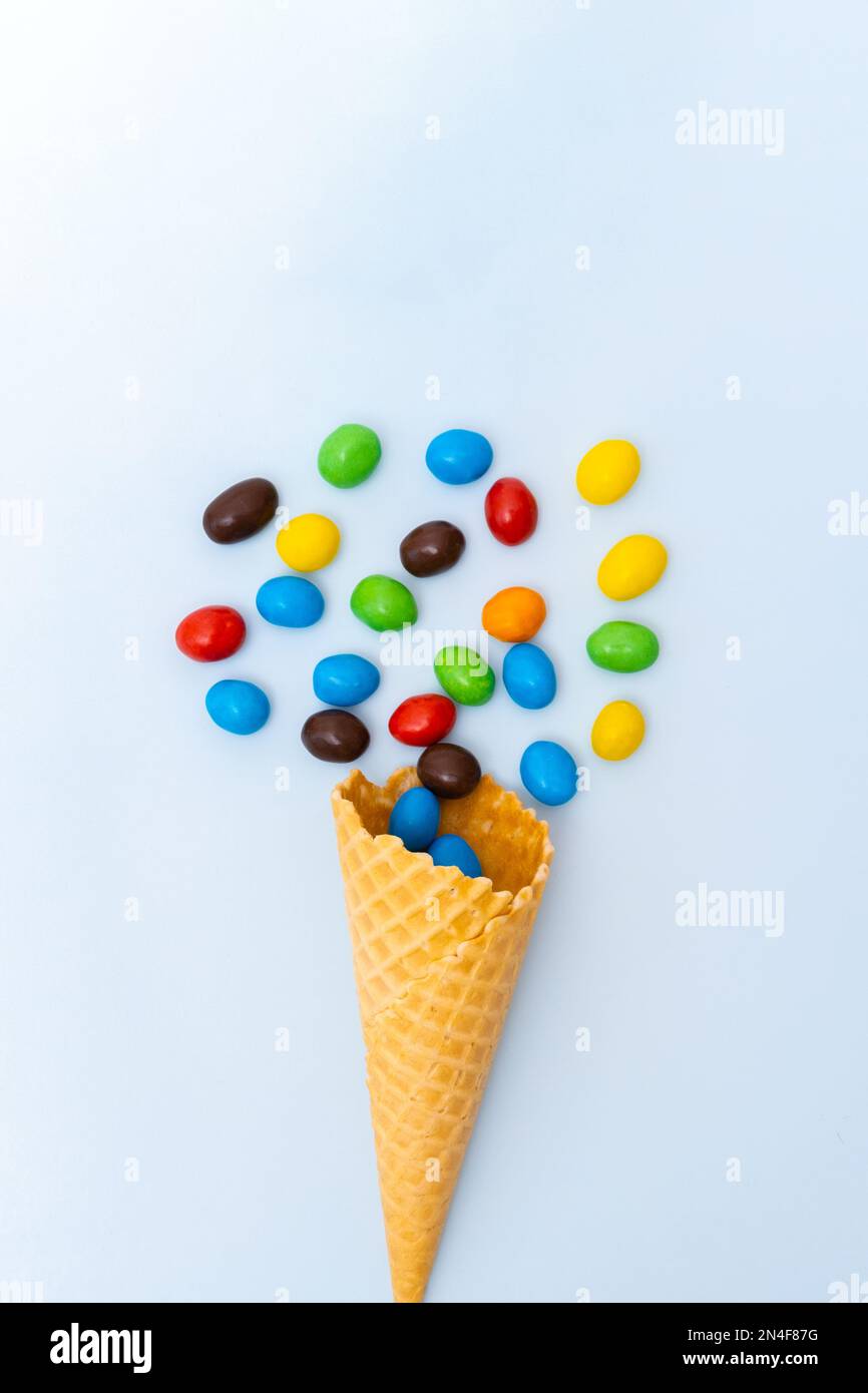 Un cône de gaufre conique vide et des bonbons ronds multicolores, des dragées, de petits œufs sur fond bleu, un cadre vertical. Des vacances agréables. Enfant Banque D'Images