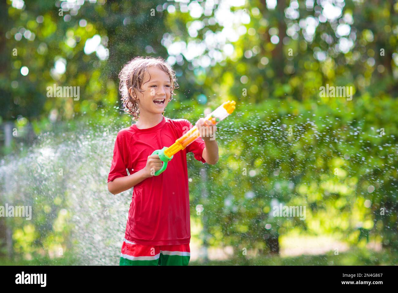 Les enfants jouent avec un tuyau d'arrosage. Jardin d'été, activités de  plein air pour les enfants. Garçon éclaboussant de l'eau par beau temps  chaud. Arrosage des plantes par les enfants dans l'arrière-cour