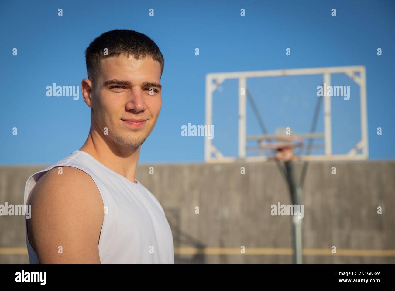 Un joueur de basket-ball souriant sur un terrain de basket-ball avec un panier derrière lui. Banque D'Images