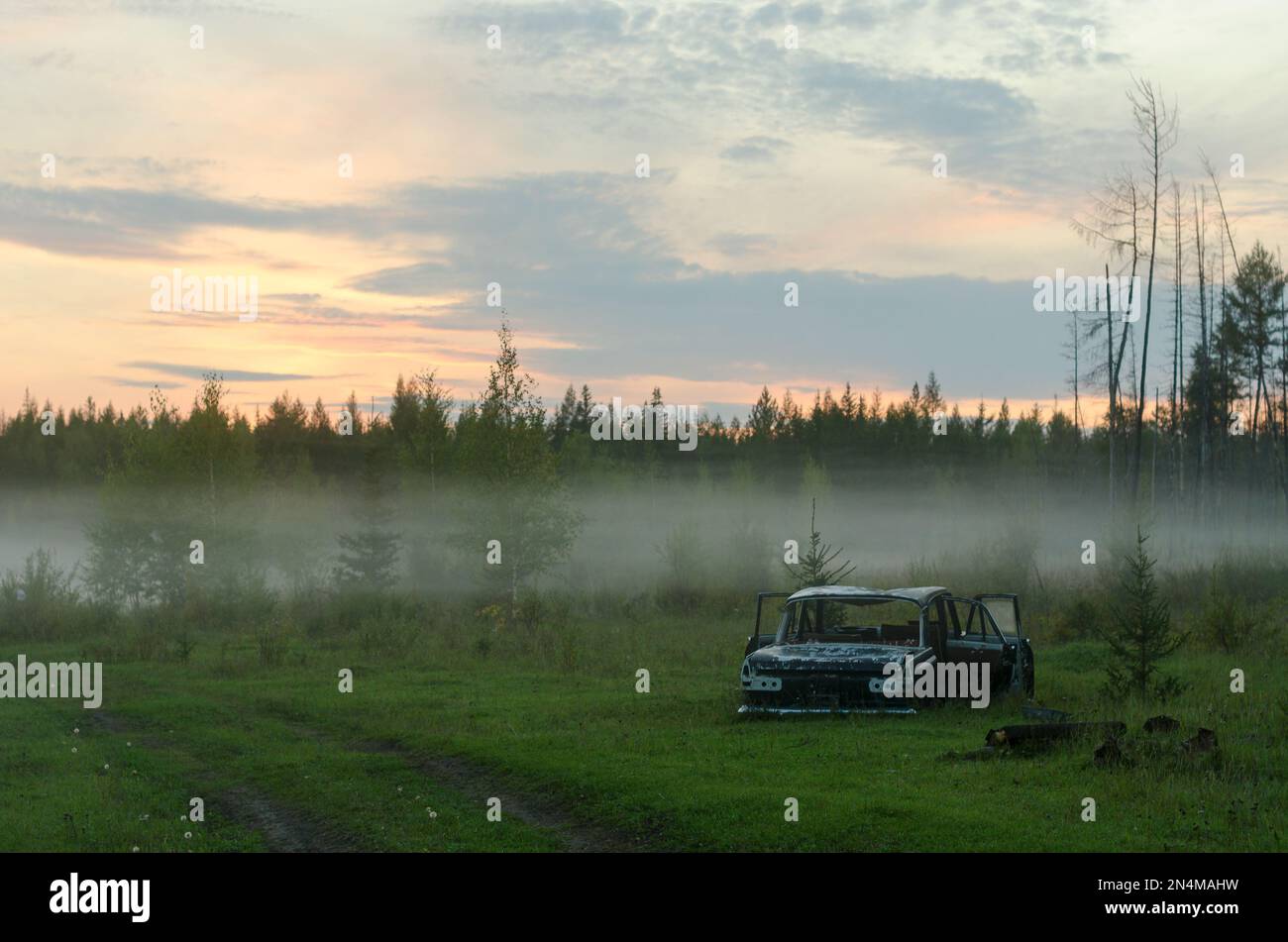 Les restes rouillés de la voiture de fer soviétique se trouvent dans la forêt près de la route dans une bande de brouillard au coucher du soleil dans le nord de la taïga de Yakut. Banque D'Images