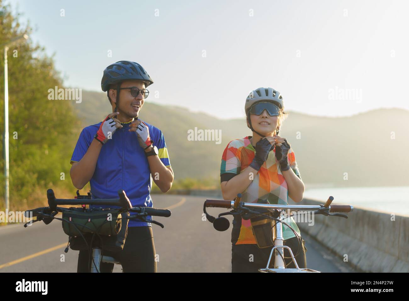 Les couples de cyclistes asiatiques mettent des casques et des mentonnières pour se préparer à leur balade en vélo autour d'un beau lac le matin. Banque D'Images