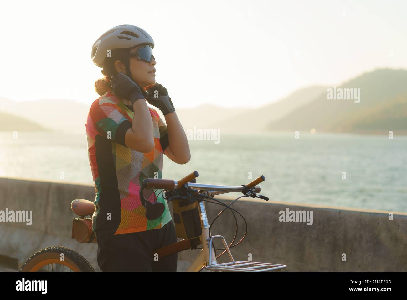 Femme asiatique cycliste portant un casque se prépare à une balade en vélo autour du lac le matin avec une belle vue sur la montagne en arrière-plan. Banque D'Images