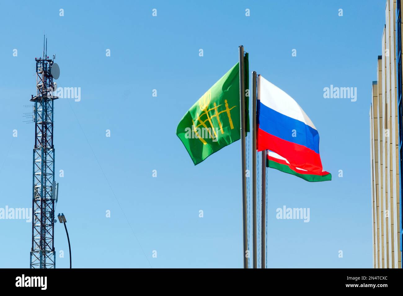 Trois drapeaux de Russie, Yakutia et Suntara se développent dans le vent sur le fond d'une tour de radio près du bâtiment de l'administration. Banque D'Images