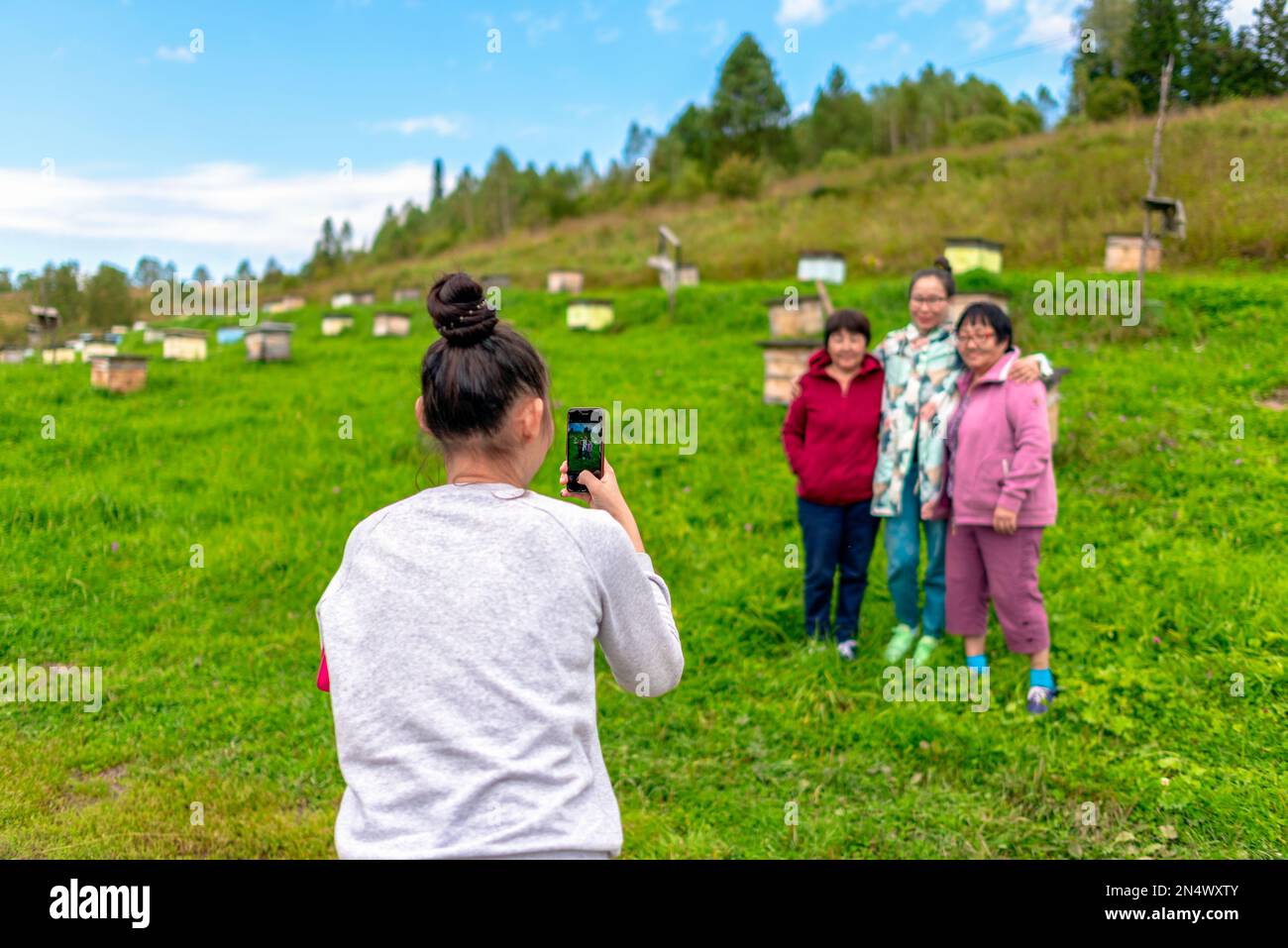 Une fille prend des photos sur un téléphone gadget Yakut famille mère et soeur et une jeune fille posent main dans la main sur le fond de ruches pour les abeilles o Banque D'Images