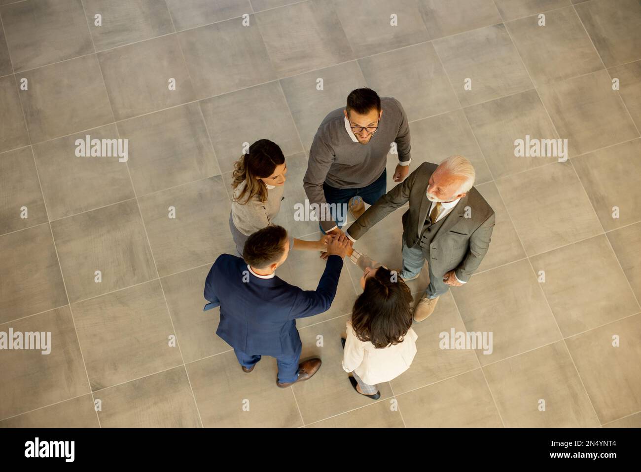Un groupe de jeunes gens d'affaires et de personnes âgées se réunissent dans un couloir de bureau, debout dans un cercle avec leurs mains jointes. Ils sont habillés de professiono Banque D'Images