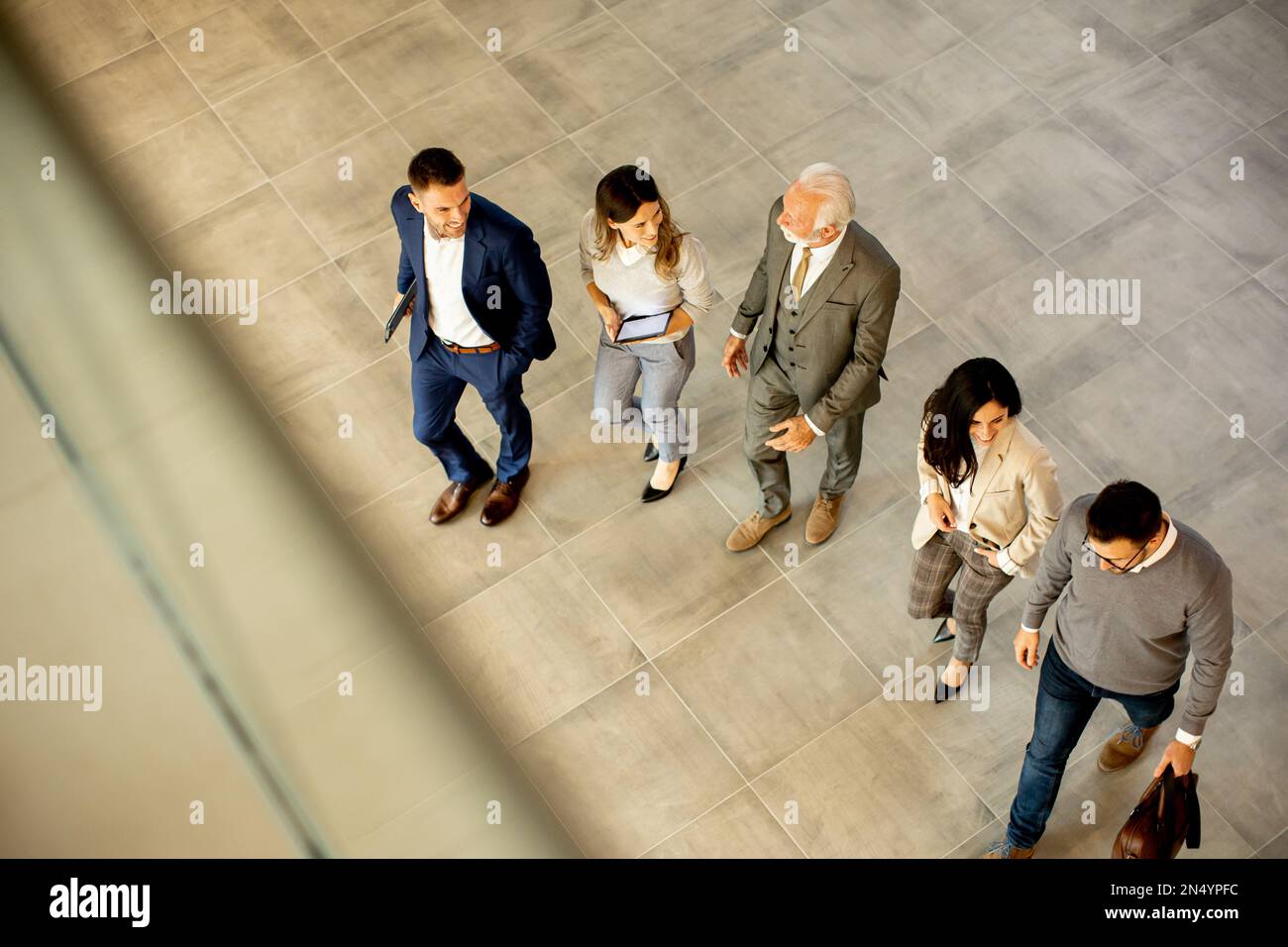 Un groupe de jeunes et de personnes âgées en voyage d'affaires se prompe dans un couloir de bureau, capturé dans une vue aérienne. Ils sont vêtus d'une tenue habillée, ils marchent avec humour Banque D'Images