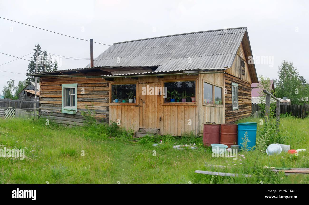 Une maison privée dans le village nord de Yakutia en bois de pin se dresse au milieu de l'herbe avec une fenêtre transparente et des pots de fleurs en automne. Banque D'Images