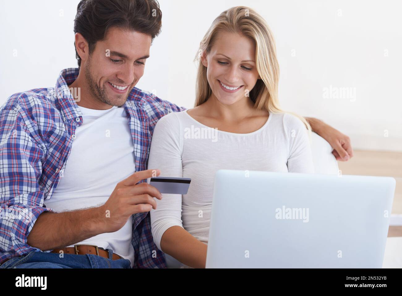 Faire du shopping dans le confort de leur maison. Un jeune couple souriant assis sur un canapé et utilisant un ordinateur portable et une carte de crédit pour acheter quelque chose en ligne. Banque D'Images