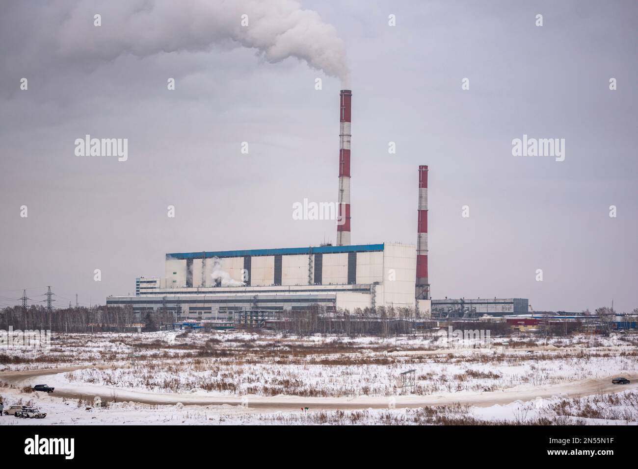 La route avec des dérives de neige et des voitures rapides va sur le fond de grandes chaudières d'une puissante centrale thermique sur la fumée de charbon dans le ciel en t Banque D'Images