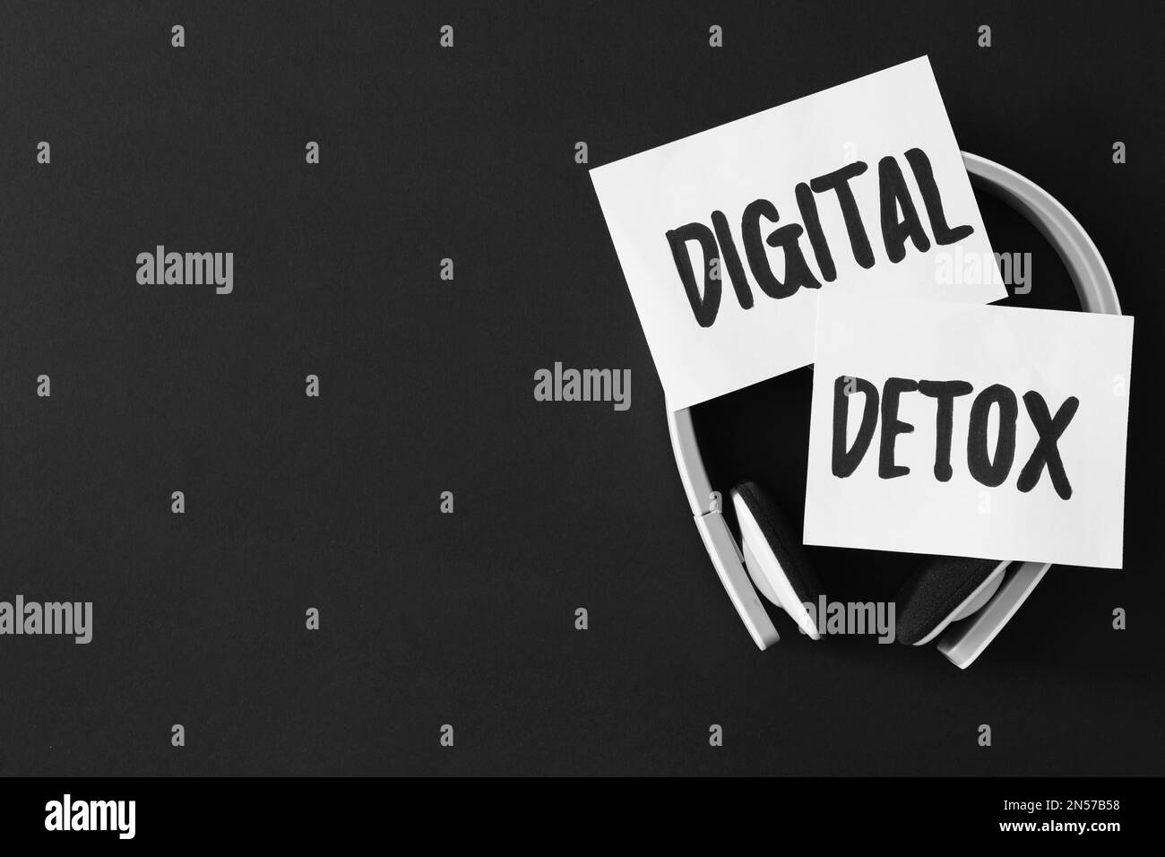 Papiers avec mots DIGITAL DETOX et écouteurs sur fond noir, vue du dessus. Espace pour le texte Banque D'Images