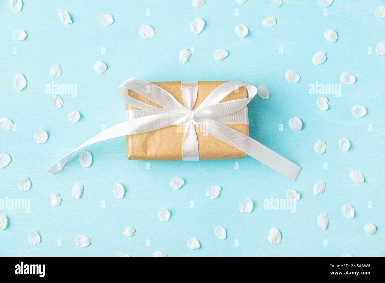 Boîte cadeau avec pétales de fleur de cerise blanche sur une table en bois bleu pastel. Mariage ou vacances. Pose à plat. Vue de dessus Banque D'Images