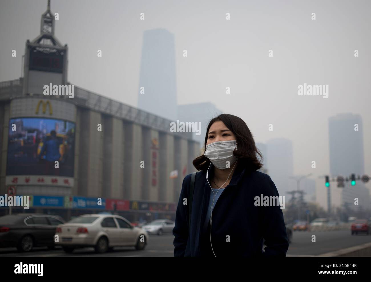 A Chinese woman wears a mask as she walks past the capital city skylines shrouded by pollution haze in Beijing Monday, March 3, 2014. (AP Photo/Andy Wong) Banque D'Images