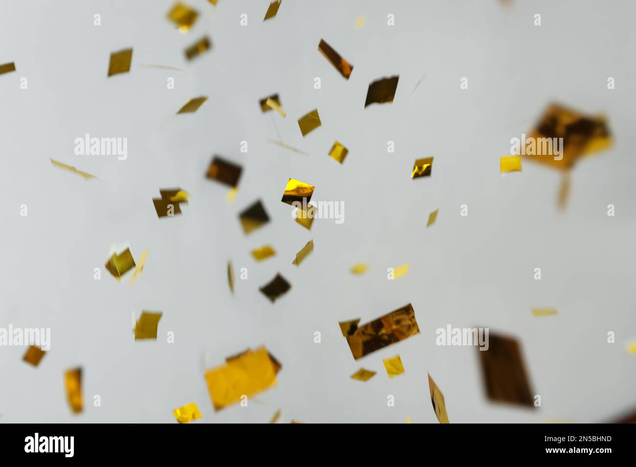Confetti dorés brillants tombant sur fond gris clair Banque D'Images