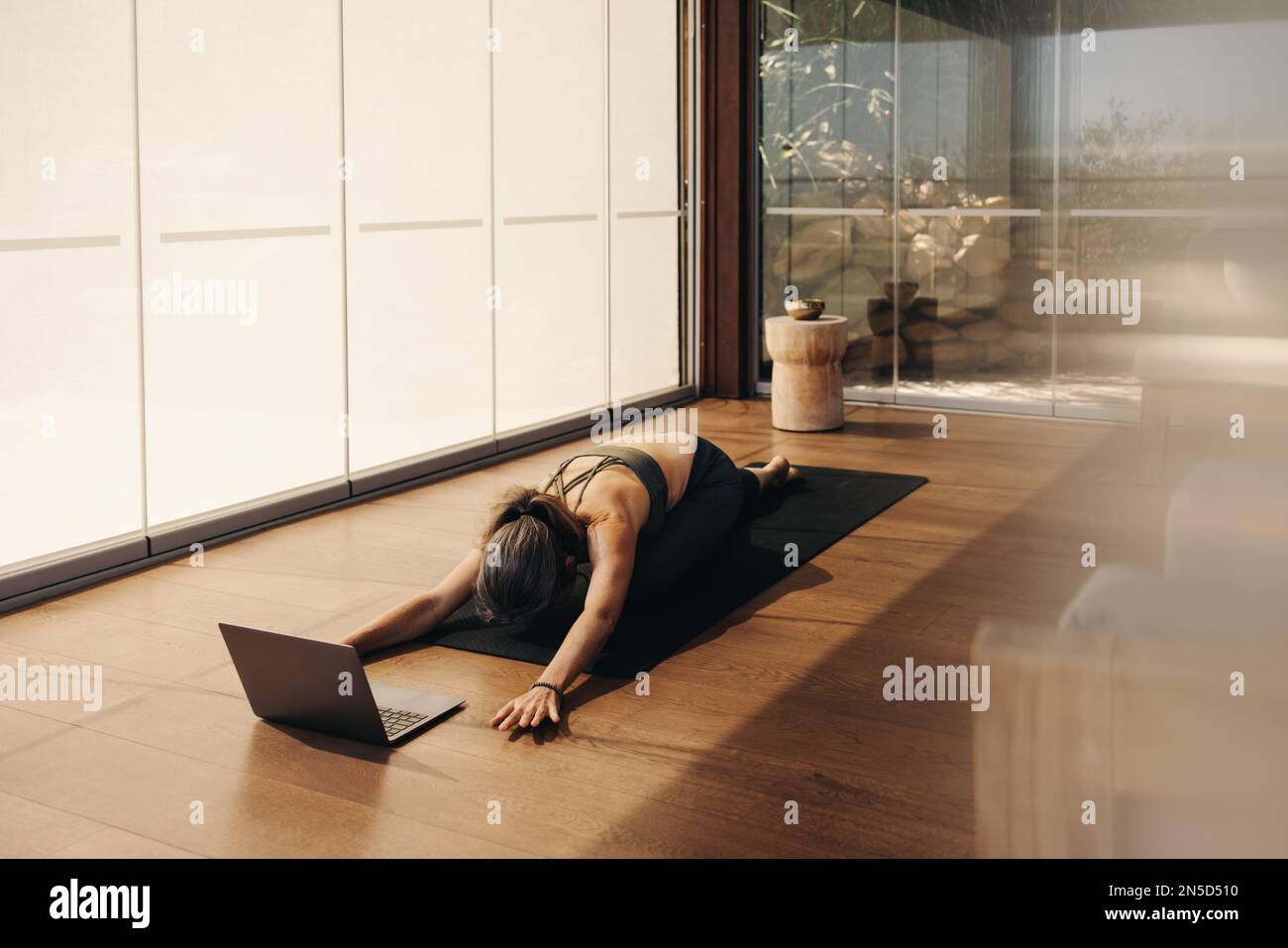 Femme faisant un exercice de pose d'enfant pendant un cours de yoga en ligne à la maison. Femme âgée pratiquant une asana agenouillée sur un tapis de yoga. Femme mature Followin Banque D'Images