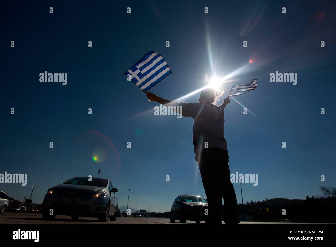 A protester raises Greek national flags to vehicles passing through without paying at the toll stations of Afidnes about 25 kilometers (12 miles) north of Athens, Sunday, Feb. 16, 2014. Hundreds of local residents of outlying Athens areas angered by new price increases for highway tolls took part in the rally. In the last couple of weeks drivers have started to pay 40-60 percent more on some sections of the Greek highway. (AP Photo/Kostas Tsironis) Banque D'Images