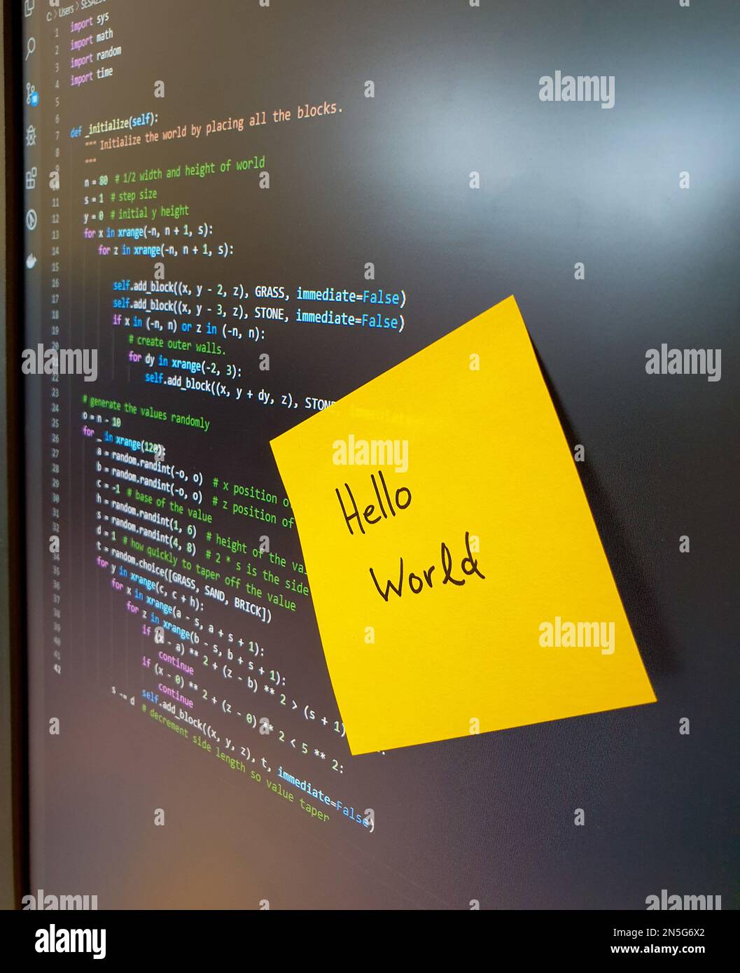 Écran d'ordinateur montrant le code python avec un autocollant jaune disant bonjour monde Banque D'Images