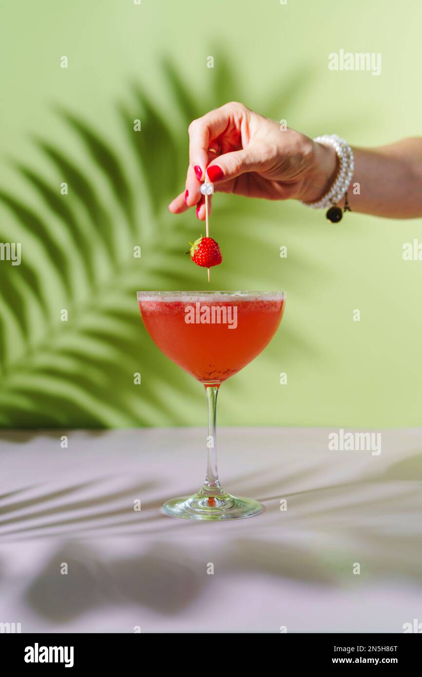 La main d'une femme met des fraises dans un cocktail Rossini. Banque D'Images