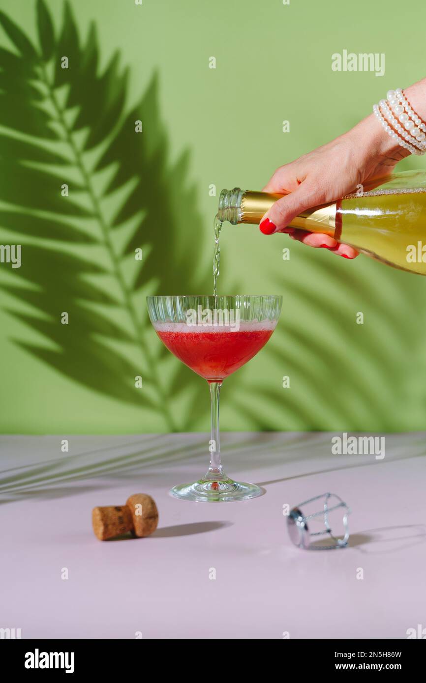 Une main de femme avec une manucure rouge verse du champagne dans un verre. Banque D'Images