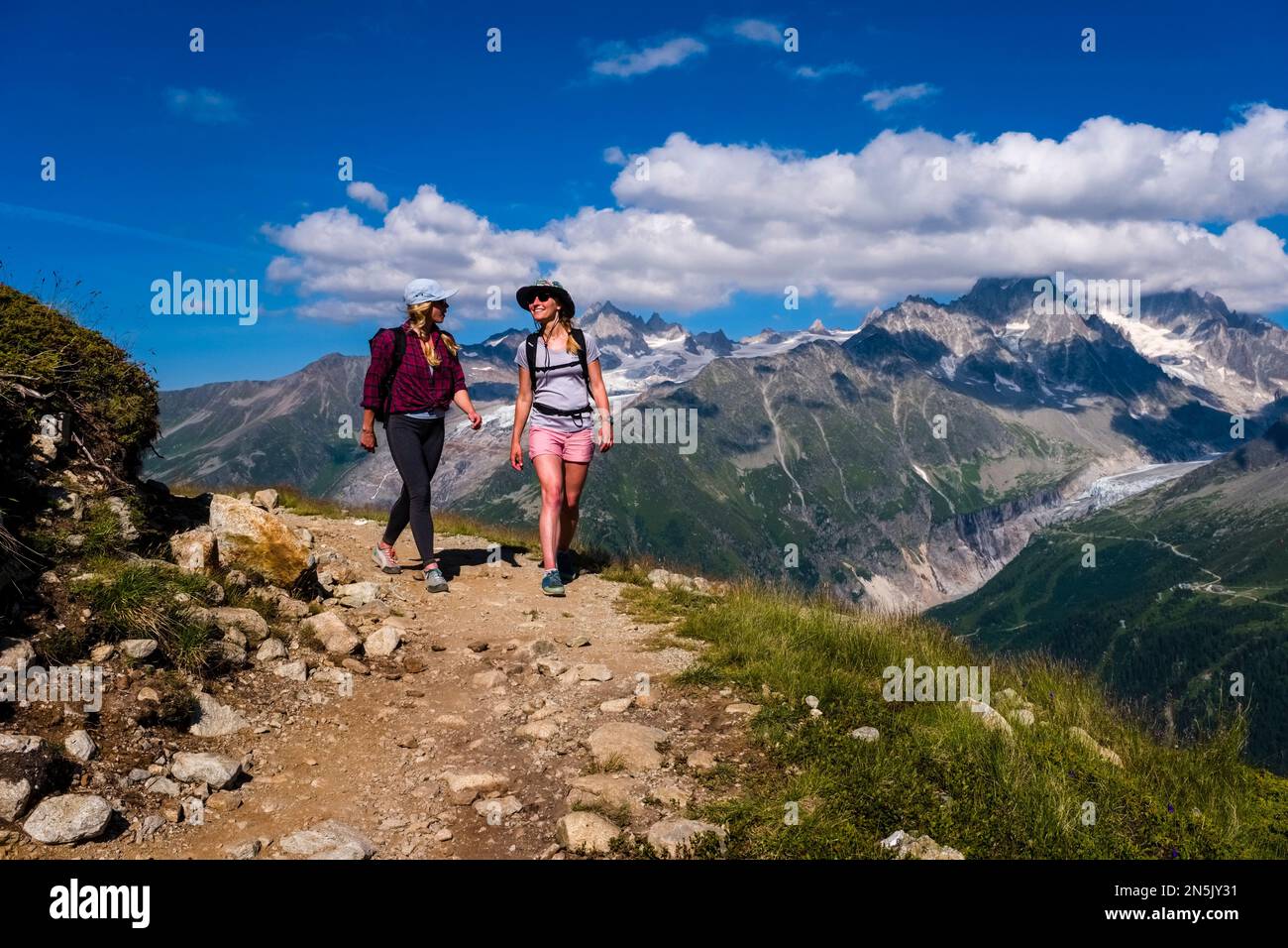 Deux jeunes randonneurs femelles marchant sur un sentier près de la Flégère, les sommets de la partie est du massif du Mont blanc au loin. Banque D'Images