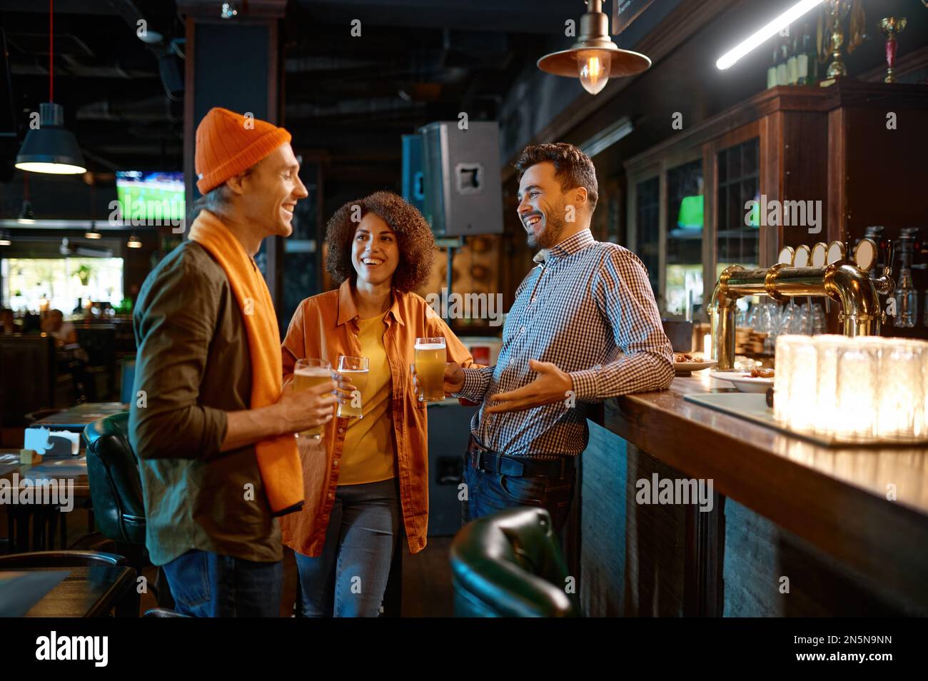Des amis heureux parlent tout en buvant de la bière au comptoir du bar Banque D'Images