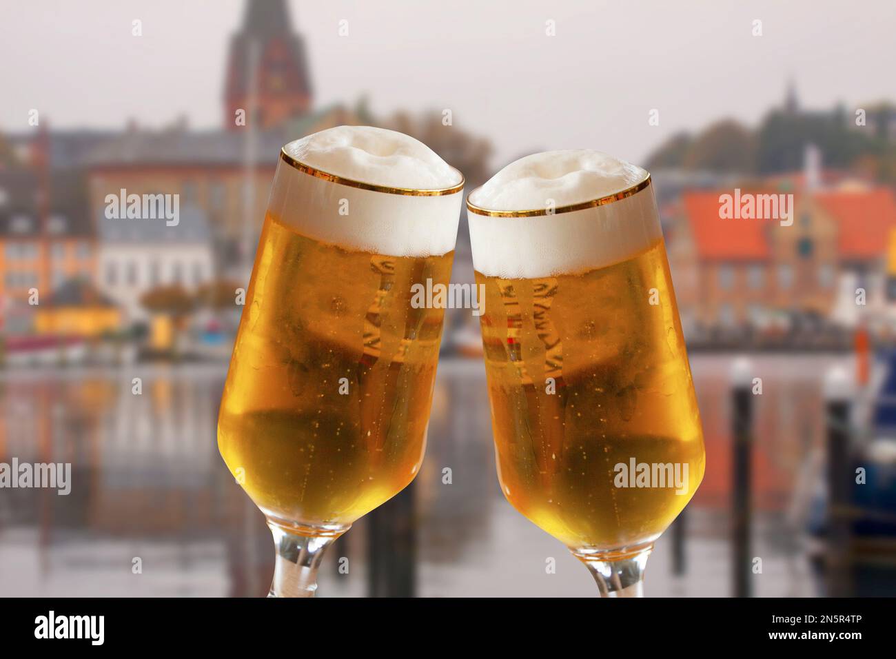Paire de verres à bière faisant un toast avec la vieille ville allemande floue en arrière-plan. Bière fraîche rafraîchissante avec mousse blanche. Banque D'Images