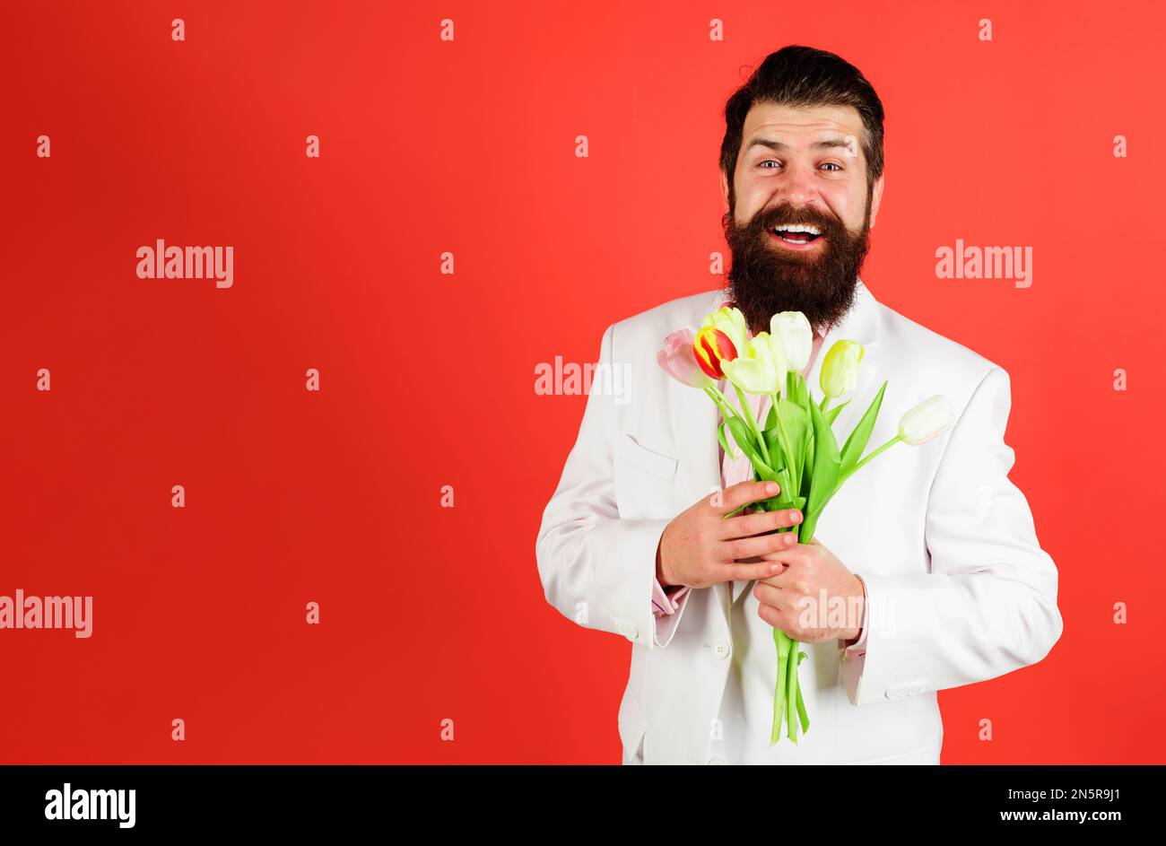 Homme barbu souriant avec bouquet de fleurs. Homme d'affaires avec bouquet de tulipes pour l'anniversaire. Homme romantique avec bouquet de fleurs de printemps. Frais Banque D'Images